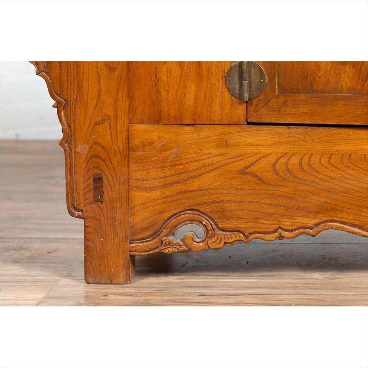 Close-up of brown elmwood two-door low cabinet with everted flanges, scrolls, and visible hinge.