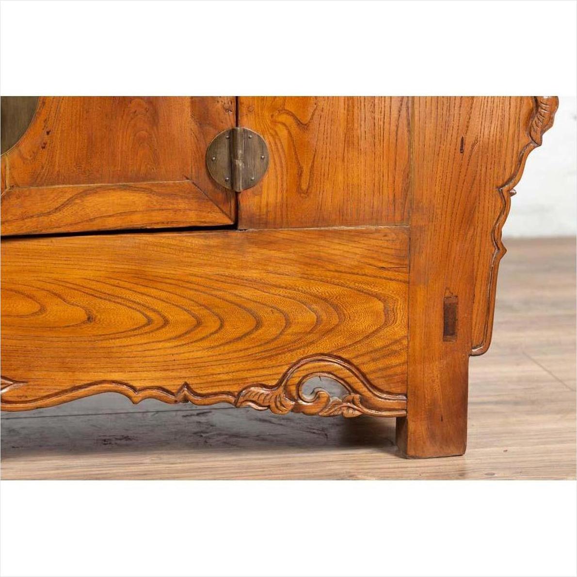 Close-up of brown elmwood low two-door cabinet with everted flanges, scrolls, and a round metal handle.