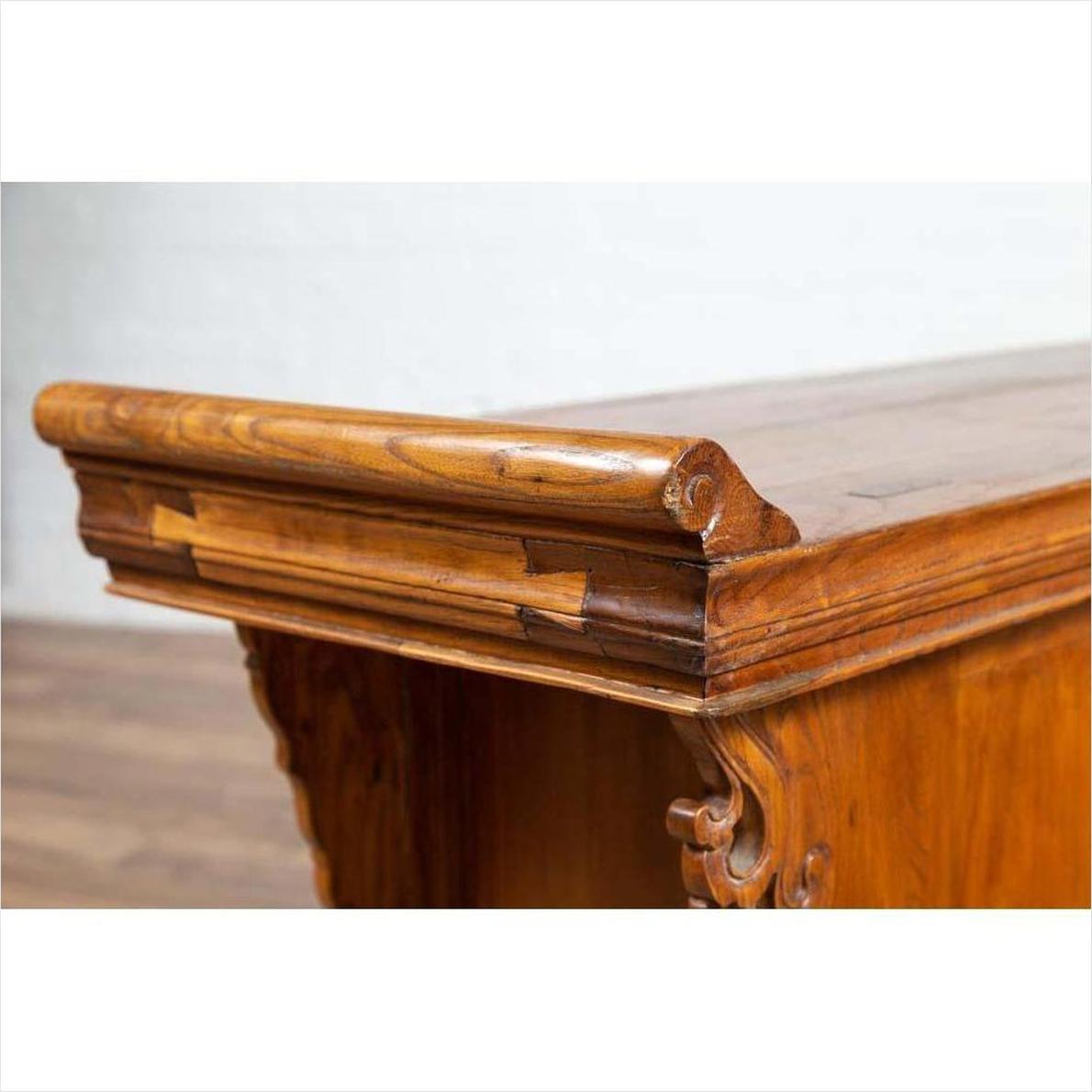 Close-up of brown elmwood two-door low cabinet with ornate scrolls, everted flanges, and carved details.