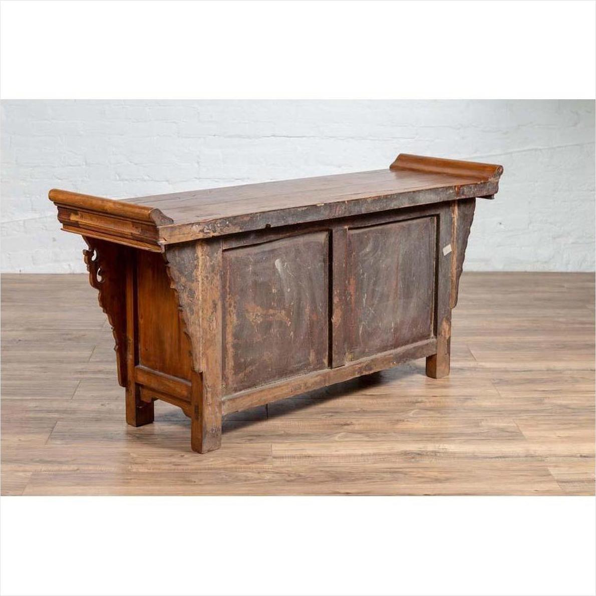 Brown elmwood low two-door cabinet with everted flanges and scrolls on a wood floor indoors.