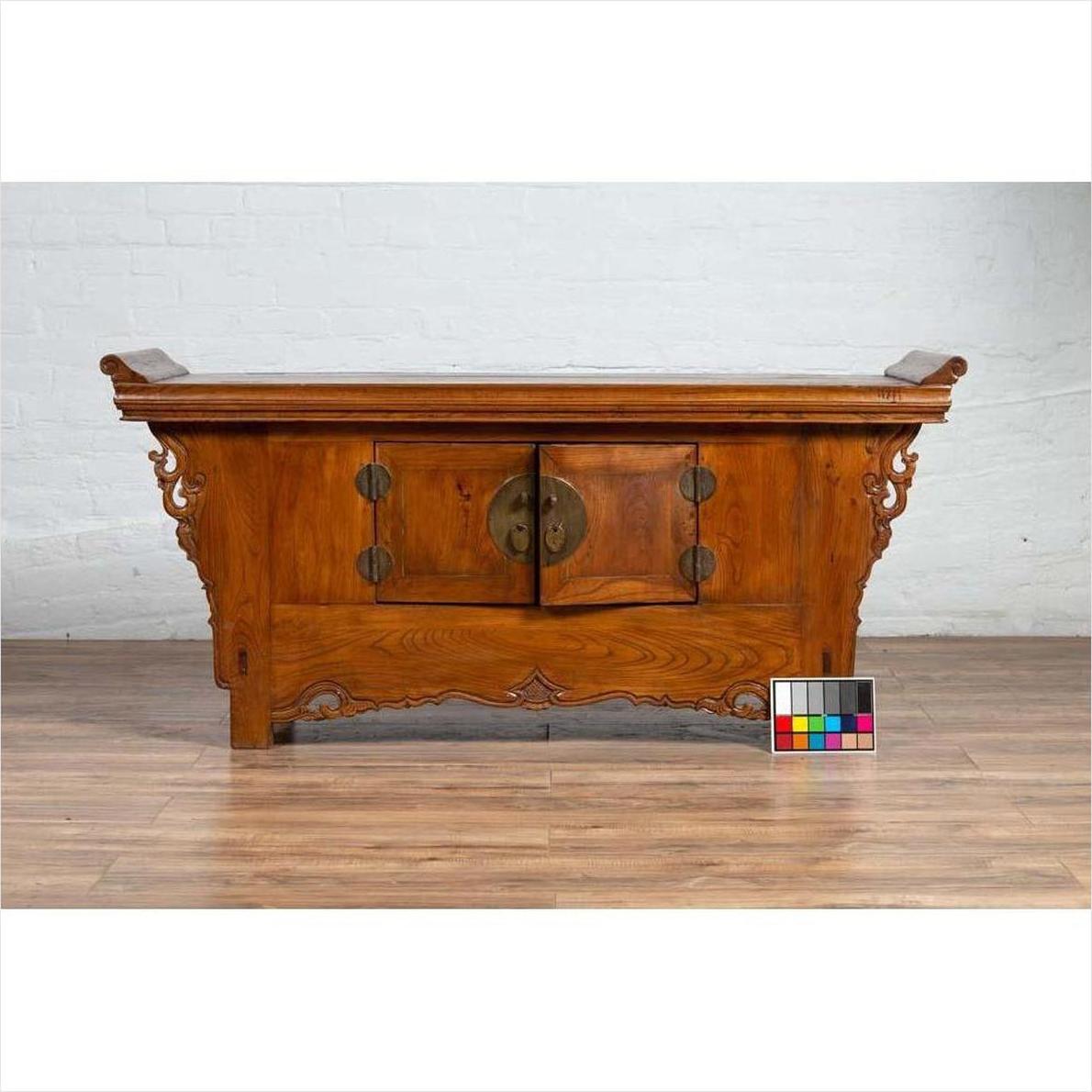 Brown elmwood two-door low cabinet with everted flanges and scrolls on wood floor next to a color chart.