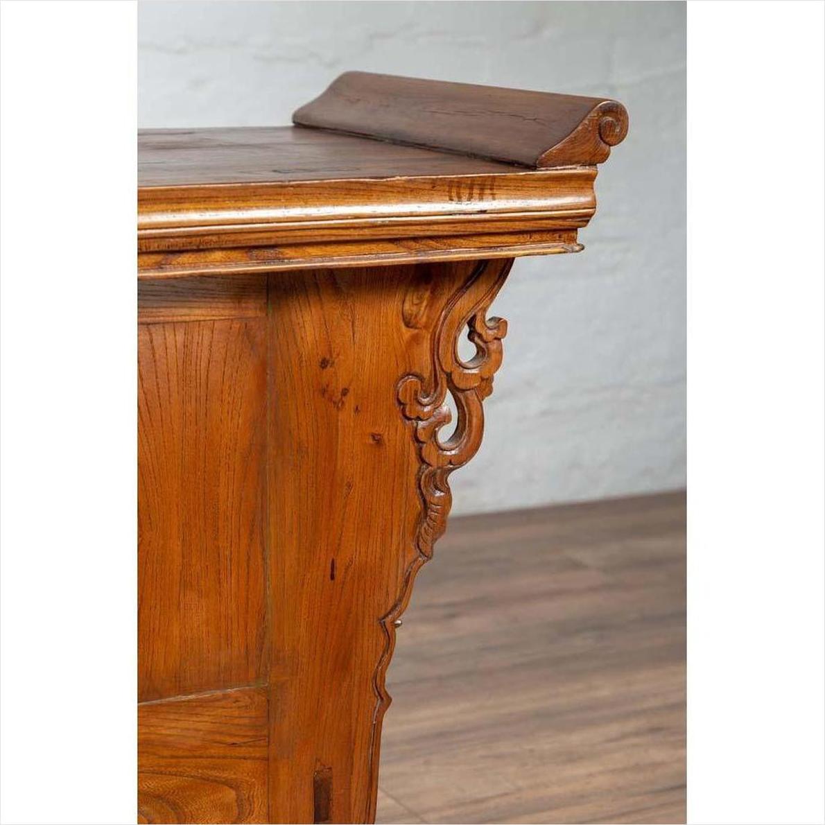 Close-up of a brown elmwood two-door low cabinet with everted flanges and scrolls on a wooden floor.