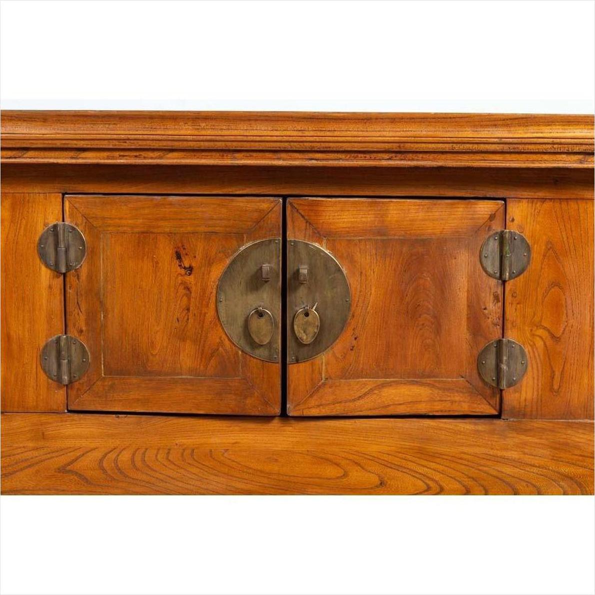 Close-up of brown elmwood cabinet doors with circular brass hardware and carved floral scrolls.