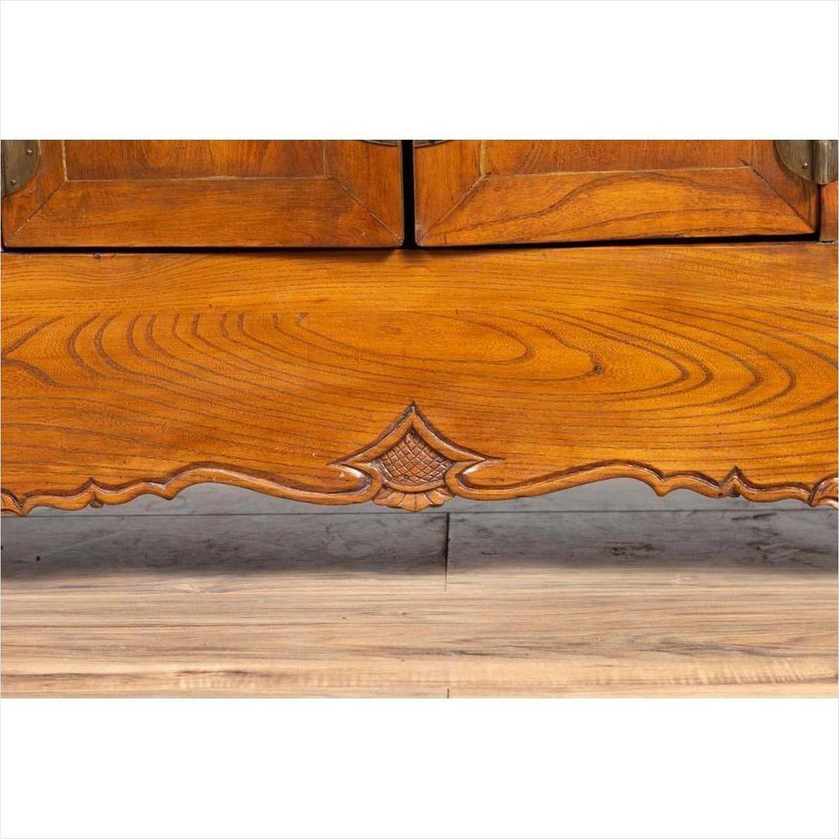 Close-up of brown elmwood two-door low cabinet with everted flanges and scrolls on a wood floor.