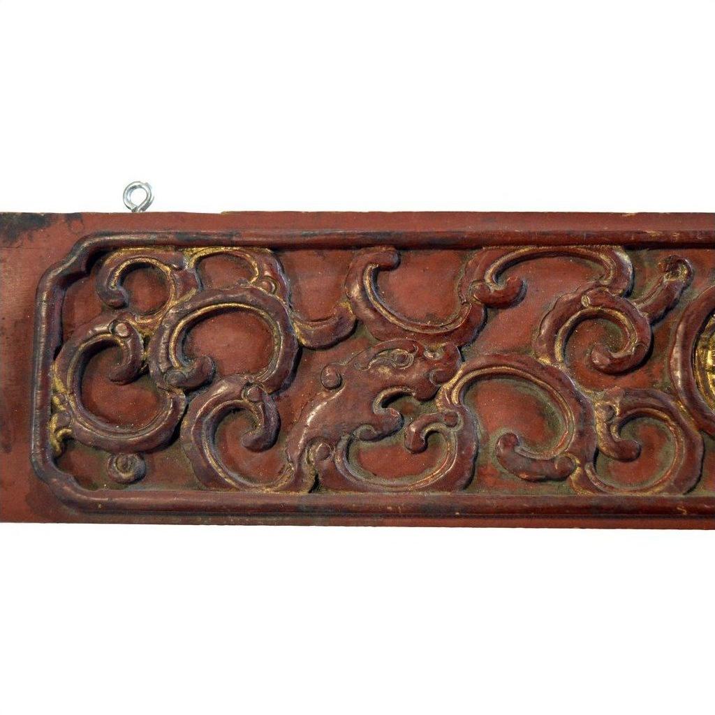 Close-up of a Chinese hand carved wood plaque featuring swirling floral patterns in muted gold and brown tones.