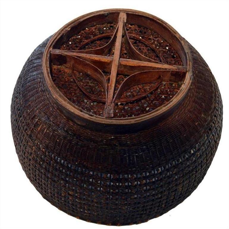 Dark lacquered bamboo basket with round shape and wooden cross-shaped lattice top, close-up on plain background.