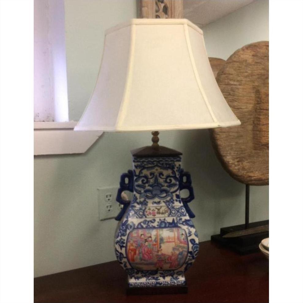 Blue and white ceramic Chinese lamp with painted scene, white shade, on wooden table.