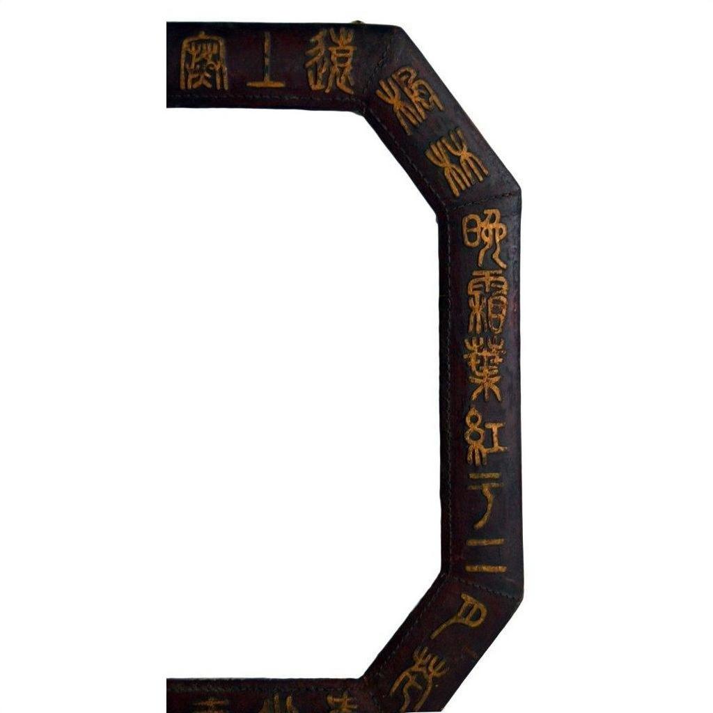 Close-up of octagonal vintage Chinese leather frame with gold calligraphy on a dark background.