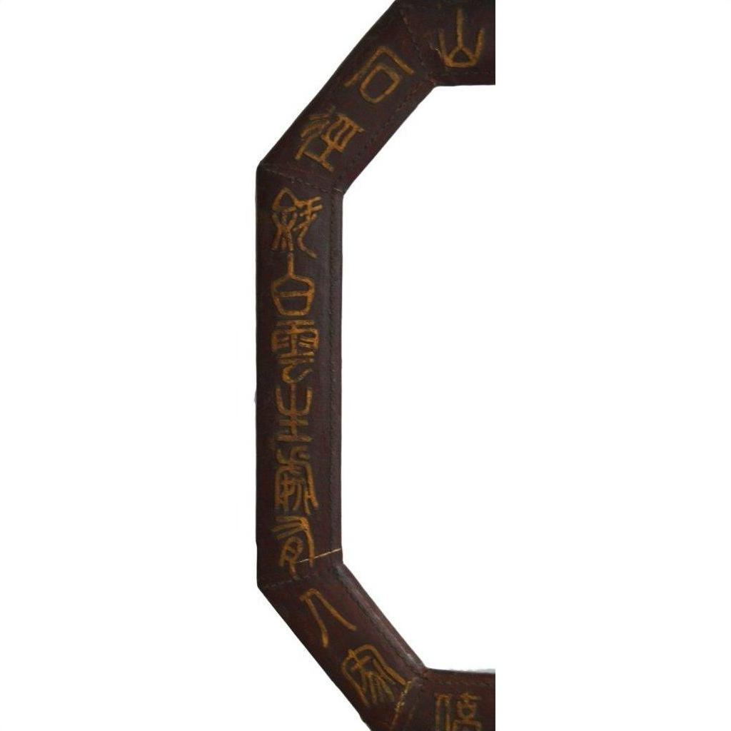 Close-up of dark wood octagonal Chinese leather frame with gold calligraphy carved along the edge.