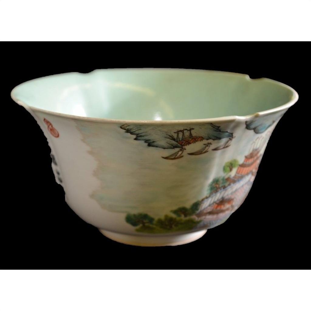 Close-up of Chinese porcelain bowl with scalloped rim, painted landscapes, cranes, and light green interior.
