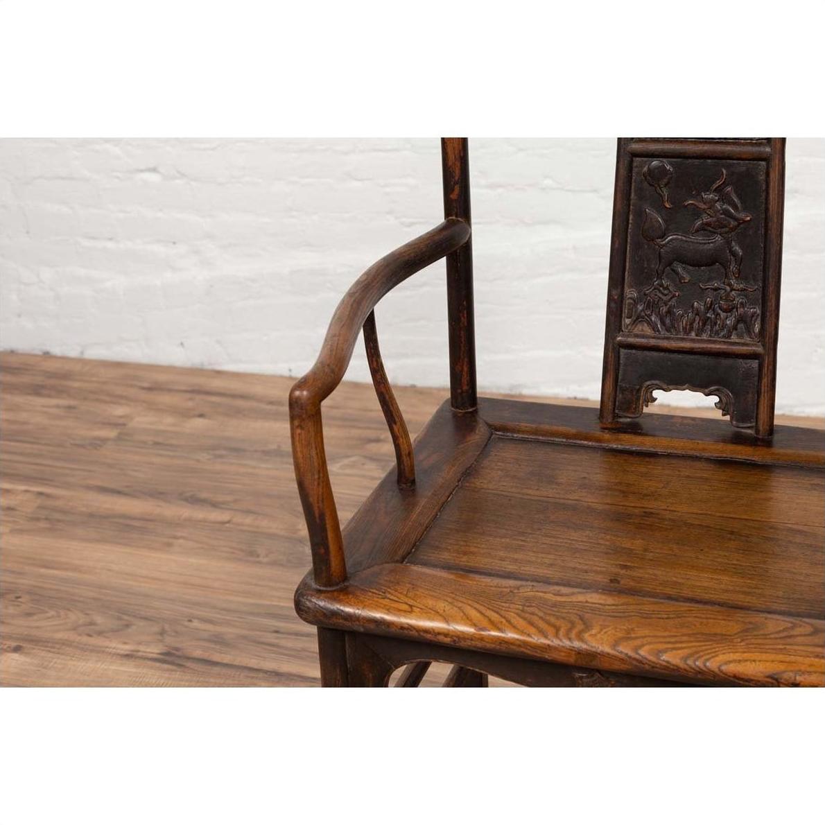 Close-up of a brown elmwood Chinese Ming Dynasty chair on a wooden floor with a white brick wall background.