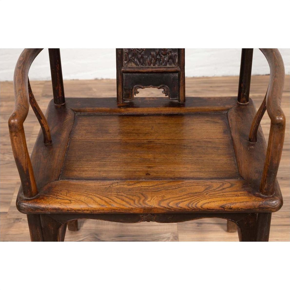 Brown elmwood Ming Dynasty chair with curved arms, carved backrest, visible wood grain on wooden floor indoors.