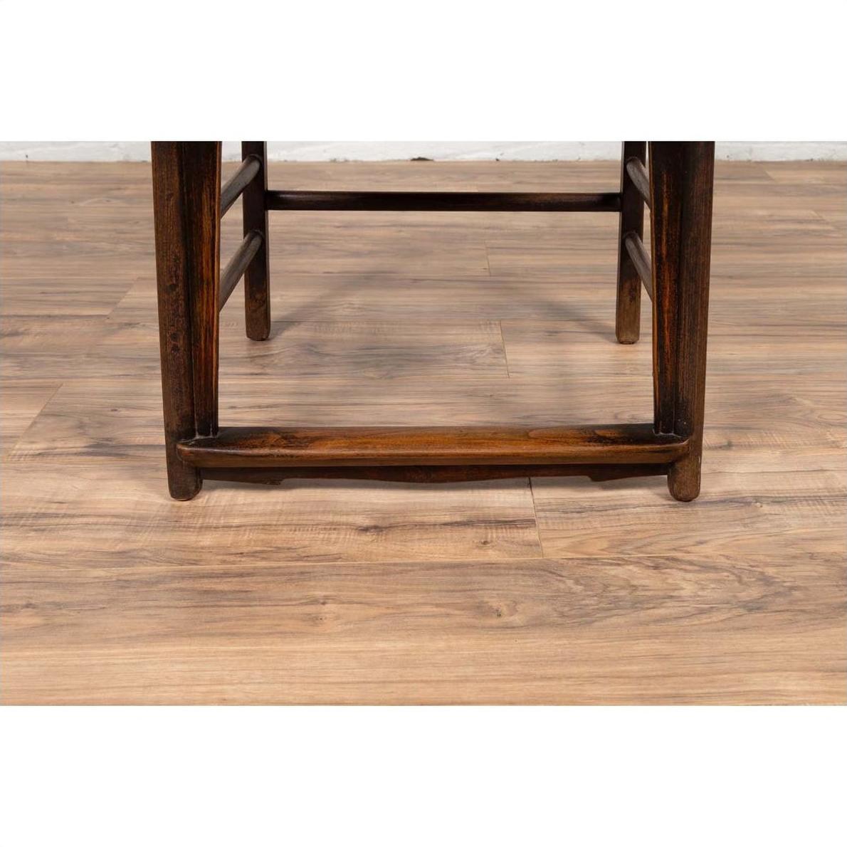 Close-up of light brown elmwood chair legs and stretcher on a light wood floor.