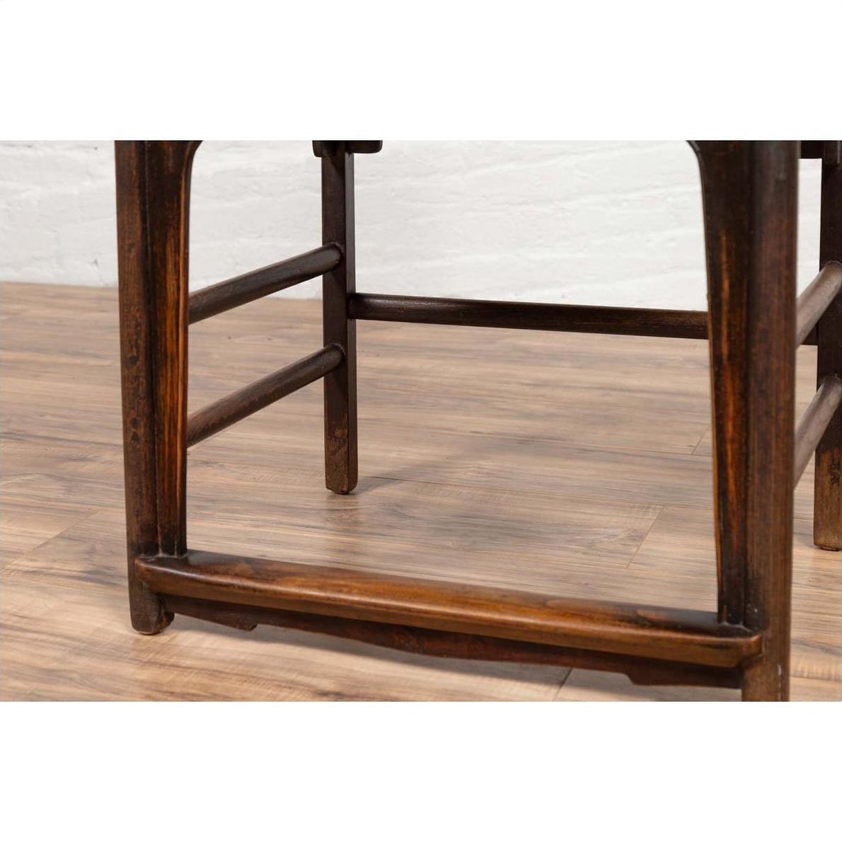 Close-up of brown elmwood Chinese Ming Dynasty chair, on light wood floor with white brick wall background.