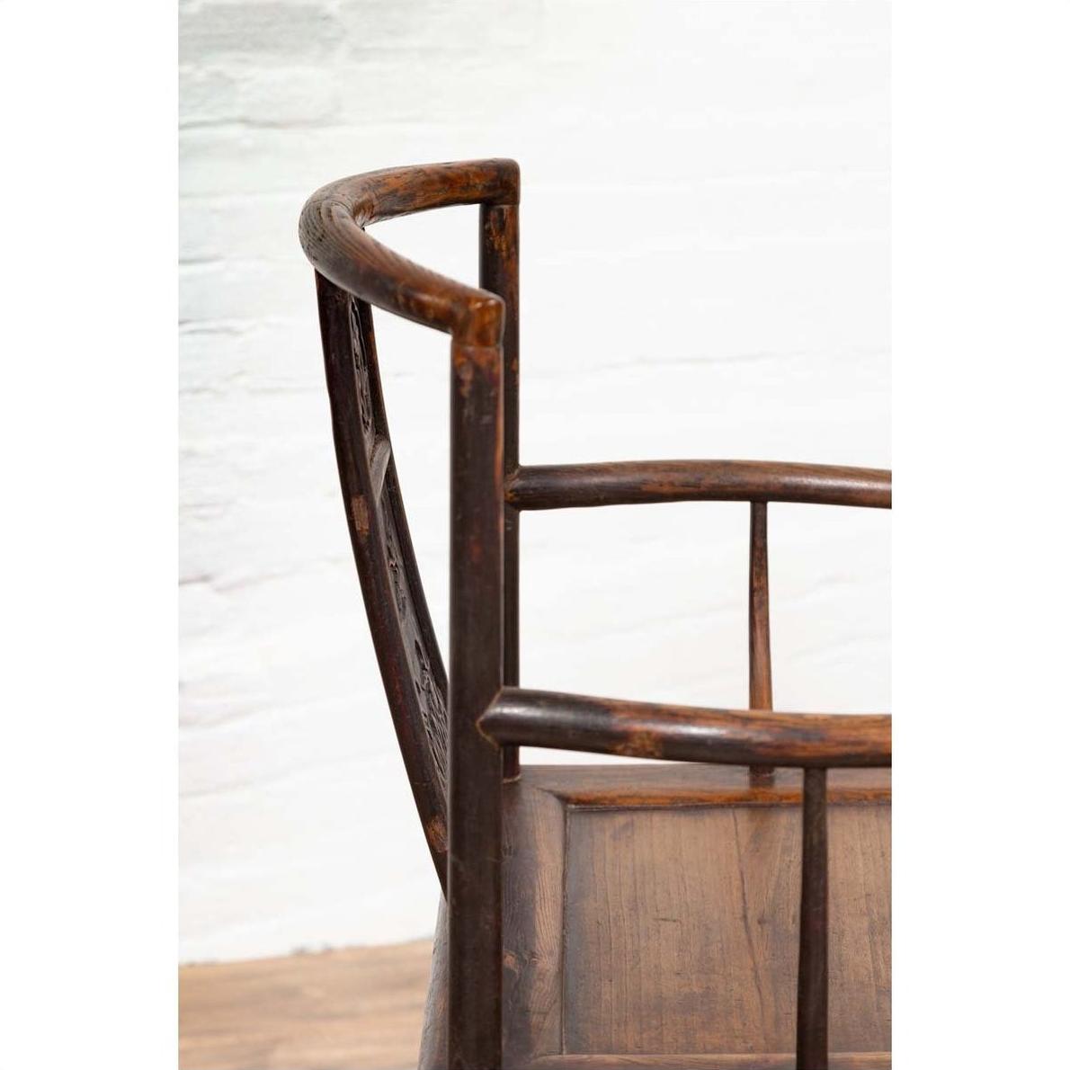 Close-up of dark wood elm Ming Dynasty chair with carved details, set against a white brick wall indoors.
