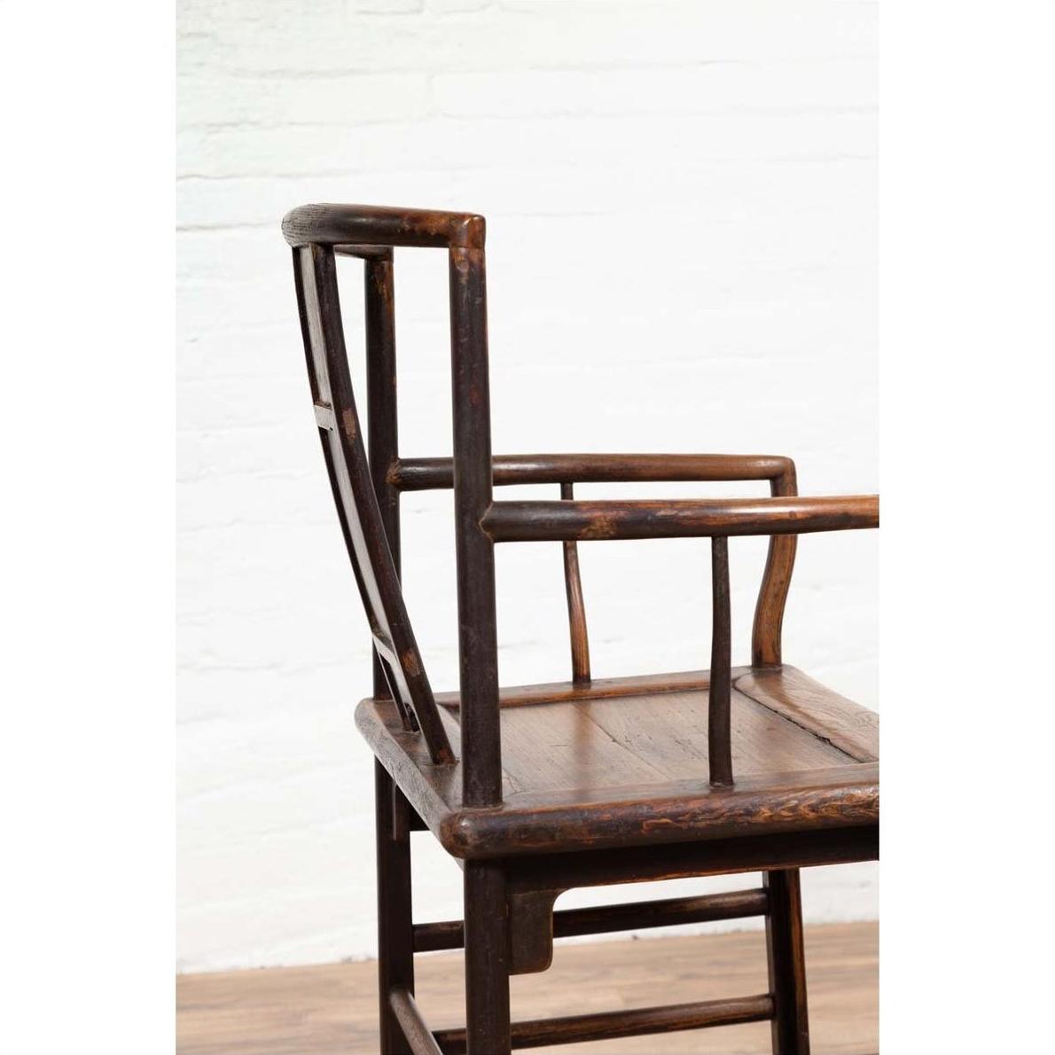 Brown elmwood Chinese Ming Dynasty chair with square backrest, side view, against white brick wall and wood floor.