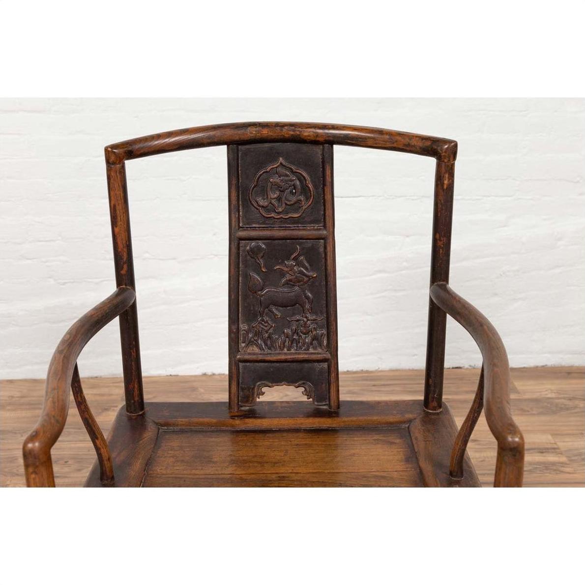 Brown carved elmwood chair with animal and floral backrest designs, positioned indoors by a white brick wall.
