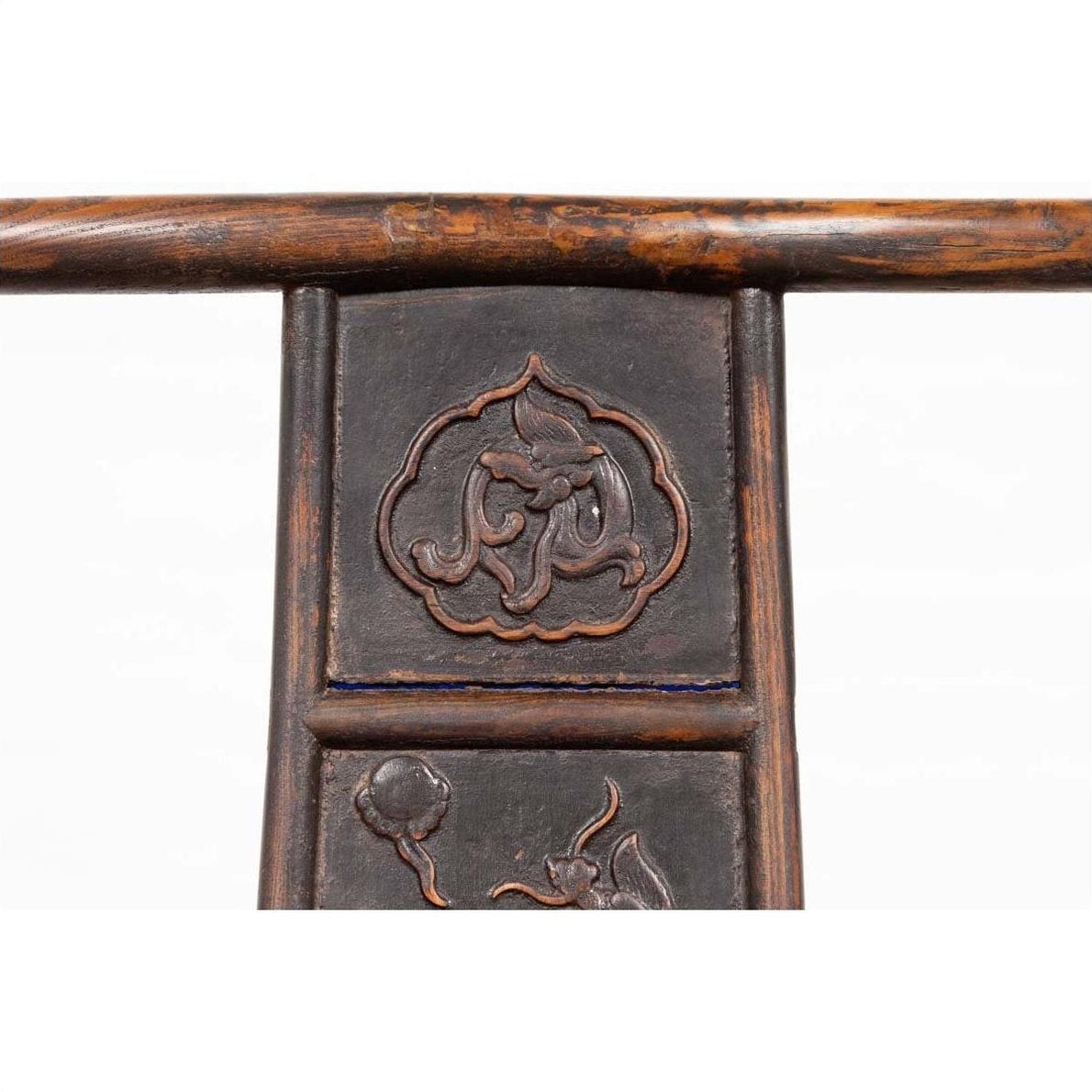 Close-up of brown elmwood Chinese Ming Dynasty chair with carved floral patterns, white background.