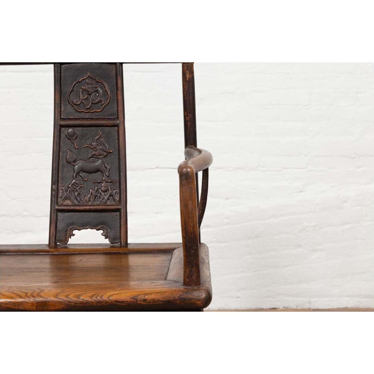 Close-up of brown elmwood Chinese Ming Dynasty chair, set indoors against a white brick wall.