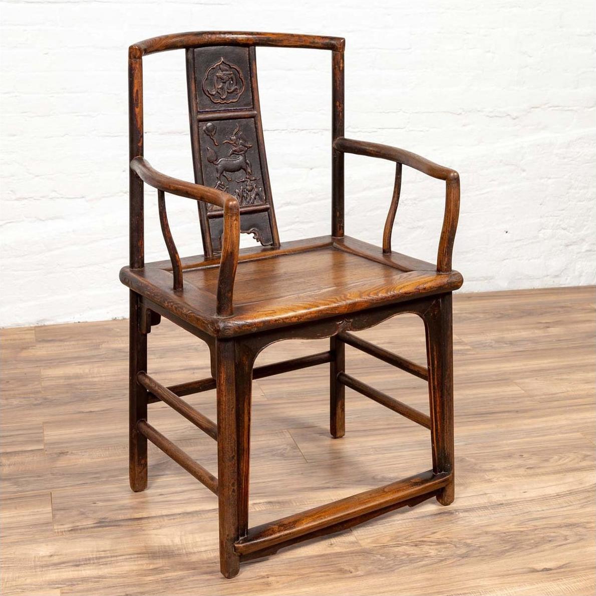 Brown elmwood chair with carved floral and animal backrest, Ming dynasty style, on a wooden floor indoors.