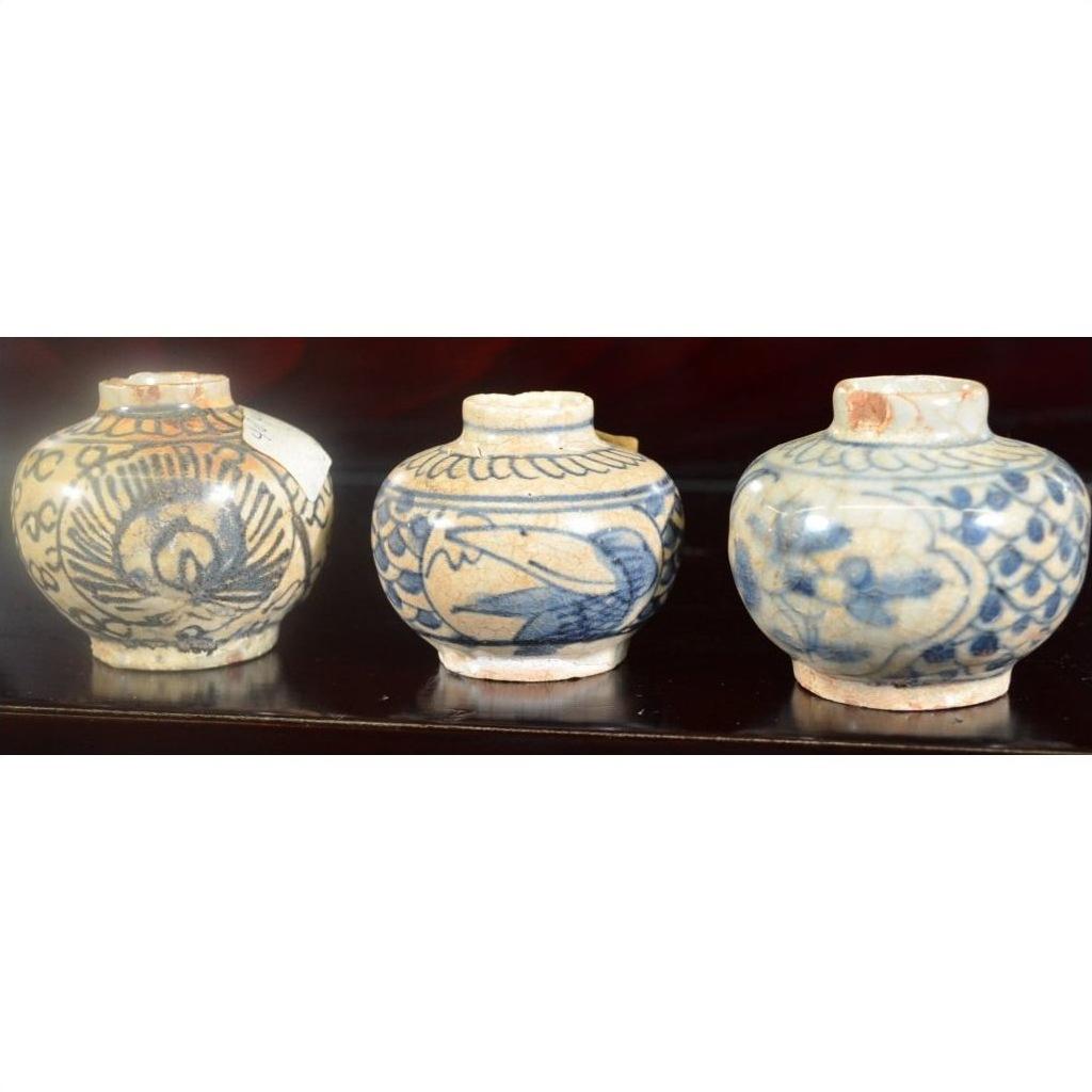 Close-up of three blue and white Chinese Ming Dynasty Swatow Ware ceramic jars on a dark wooden surface.