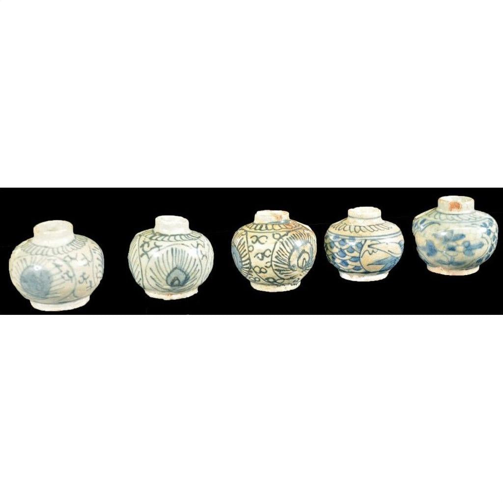 Close-up of five small round Ming Dynasty Swatow Ware jars with blue floral and geometric patterns on black.