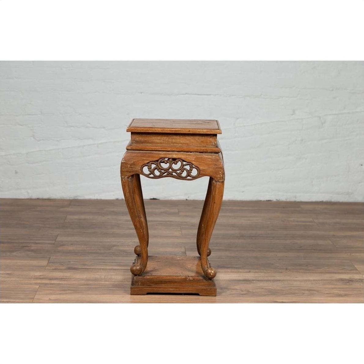 Dark wood incense stand with carved apron and cabriole legs on a wood floor against a white brick wall indoors.
