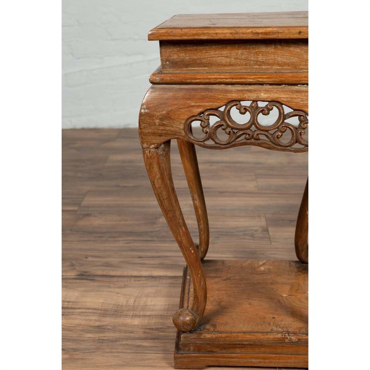 Close-up of a brown wooden Ming style incense stand with cabriole legs and carved apron, on a wood floor indoors.