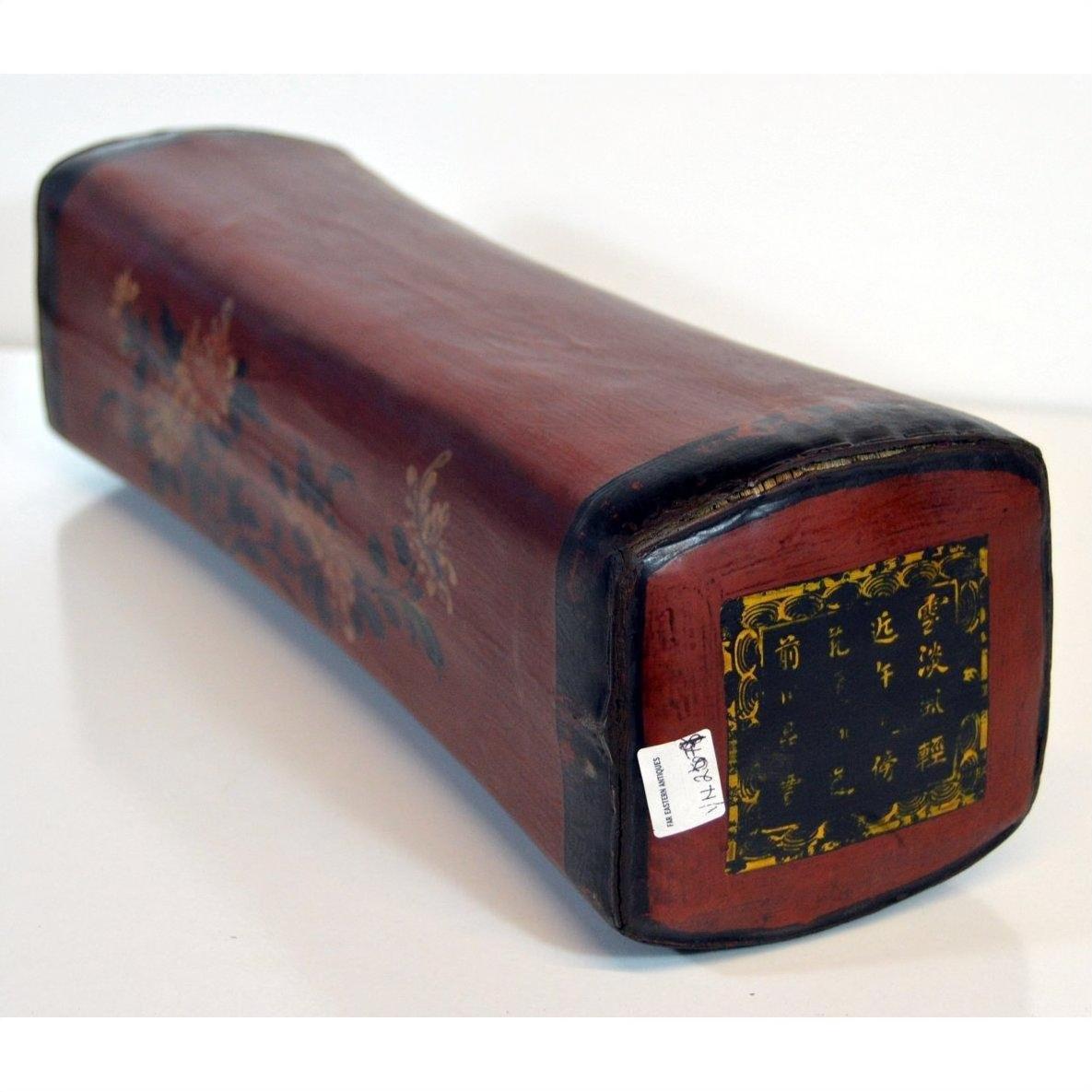 Red lacquered leather opium pillow with curved rectangular shape, floral designs, and Chinese characters on one end.