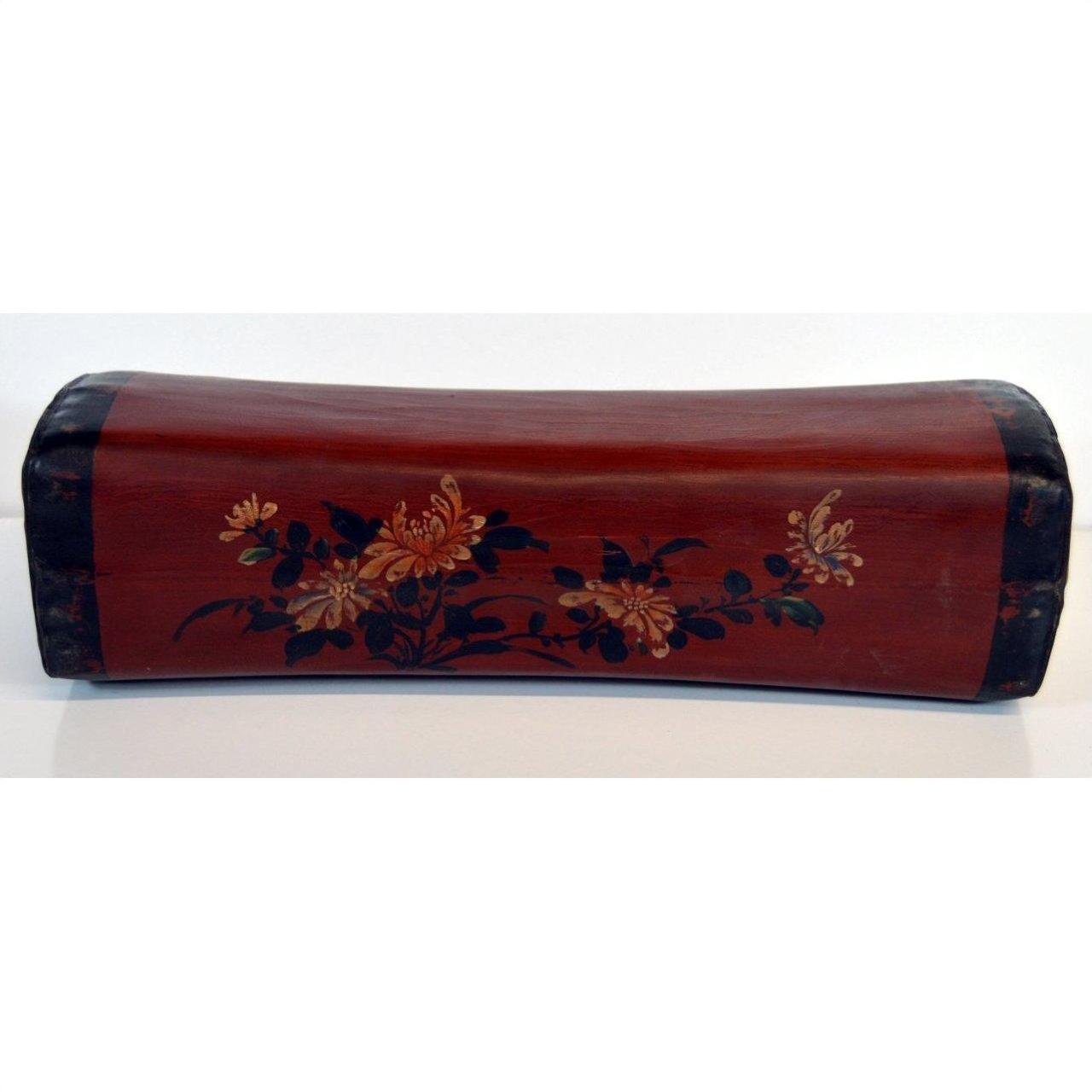 Red lacquer leather opium pillow with black ends and yellow-green floral designs, antique Chinese style, close-up view.