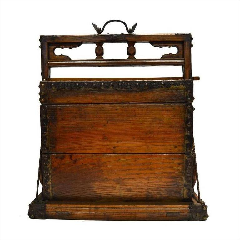 Black and brown carved wood Chinese picnic box with ornate details and metal handle, close-up on plain surface.
