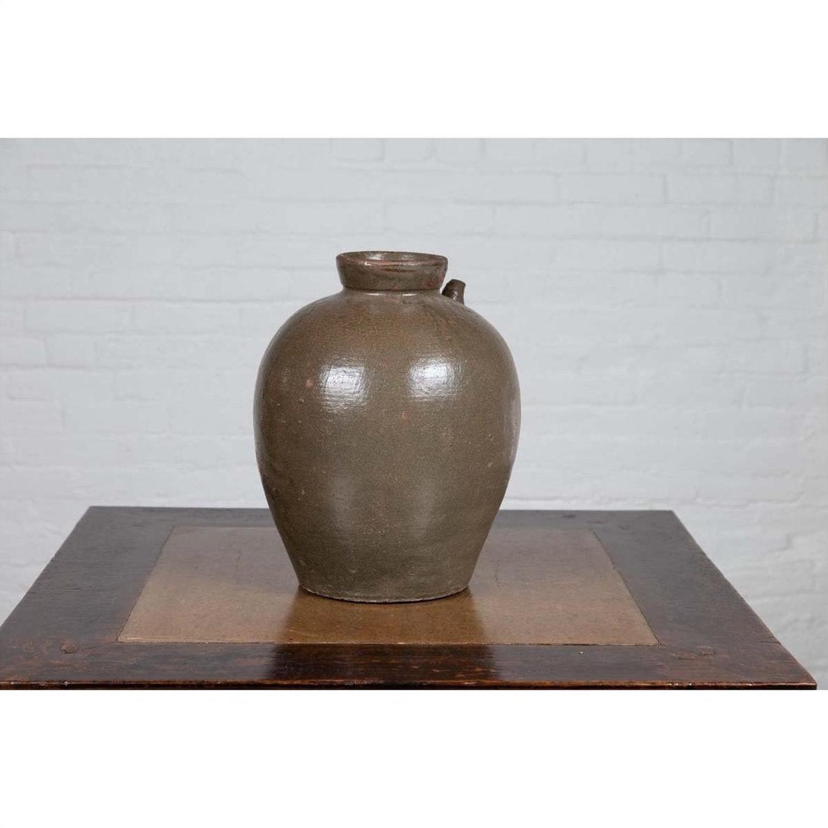 Glazed ceramic water jug with petite spout, 19th-century Qing Dynasty, on wooden table by white brick wall.