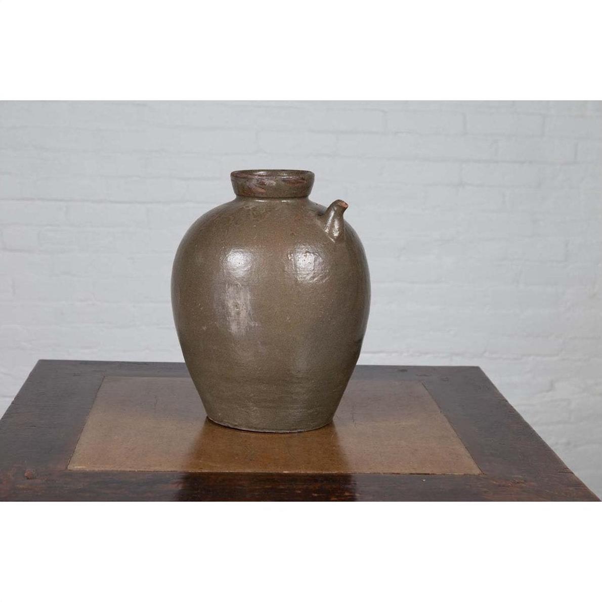 Glazed ceramic water jug with petite spout, 19th-c. Chinese Qing Dynasty, on wooden table by white brick wall.