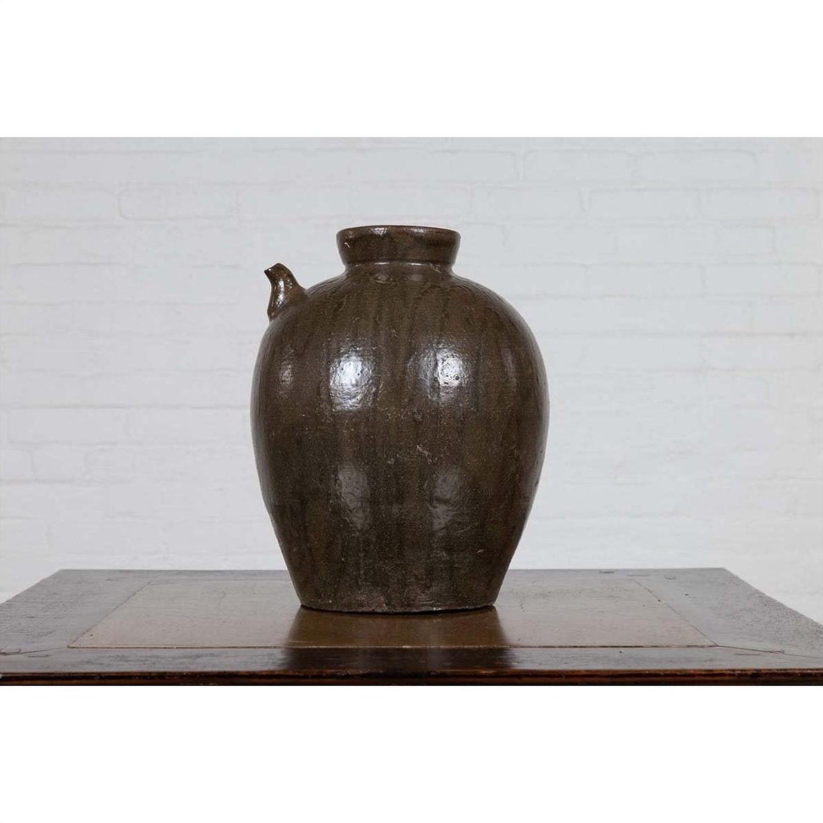 Glazed ceramic water jug with petite spout, 19th-century Qing Dynasty, on wooden table by white brick wall.