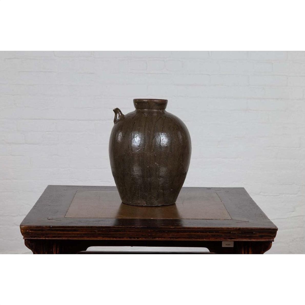 Glazed ceramic water jug with petite spout, 19th-century Qing Dynasty, on wooden table against white brick wall.