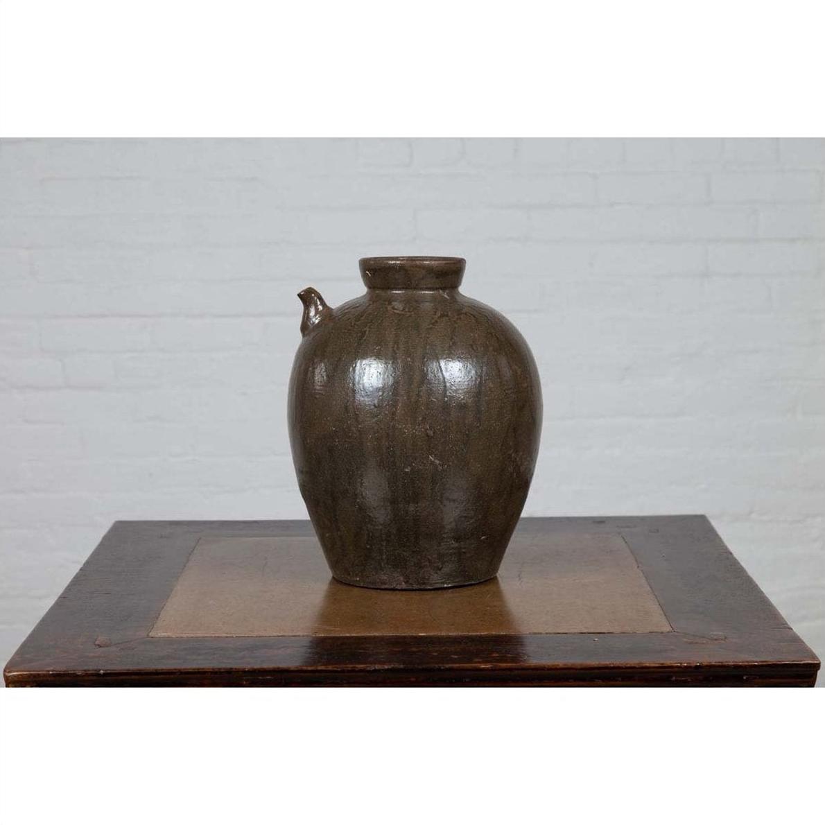 Green glazed ceramic water jug with petite spout, Qing Dynasty style, on wooden table by white brick wall.