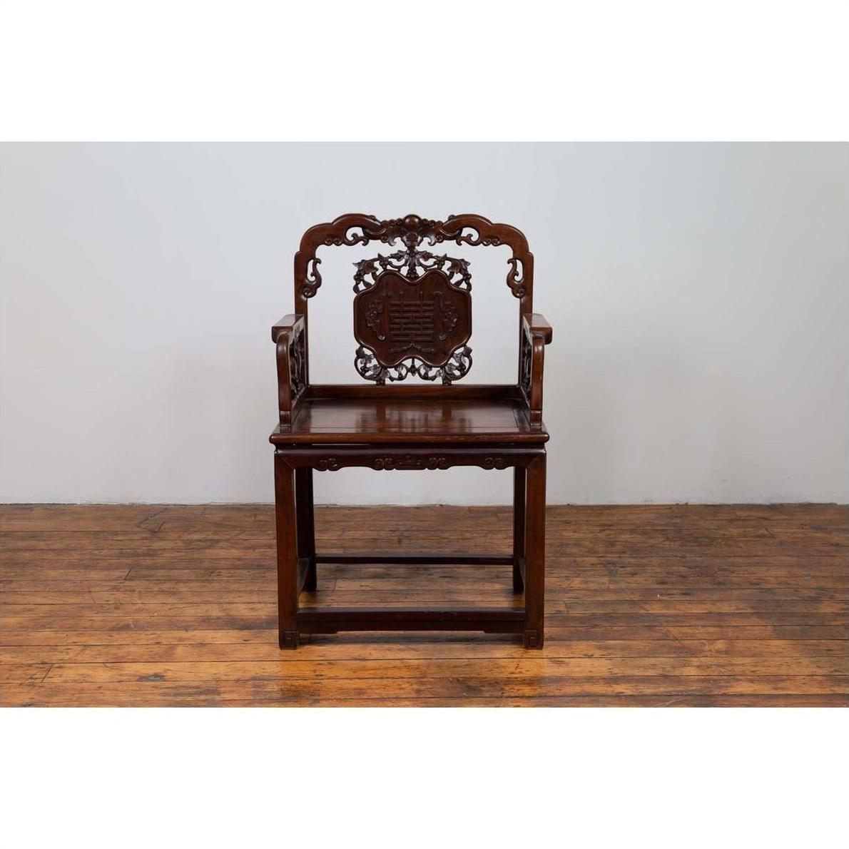 Dark rosewood Chinese chair with hand-carved backrest, 19th century, on wooden floor against plain wall.