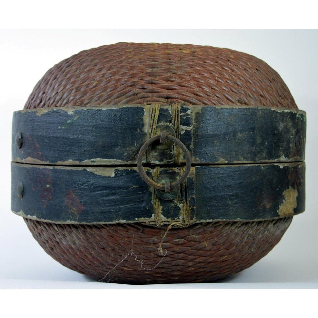 Close-up of a Chinese storage basket made of woven rattan with a black wooden band and metal ring clasp, plain background.