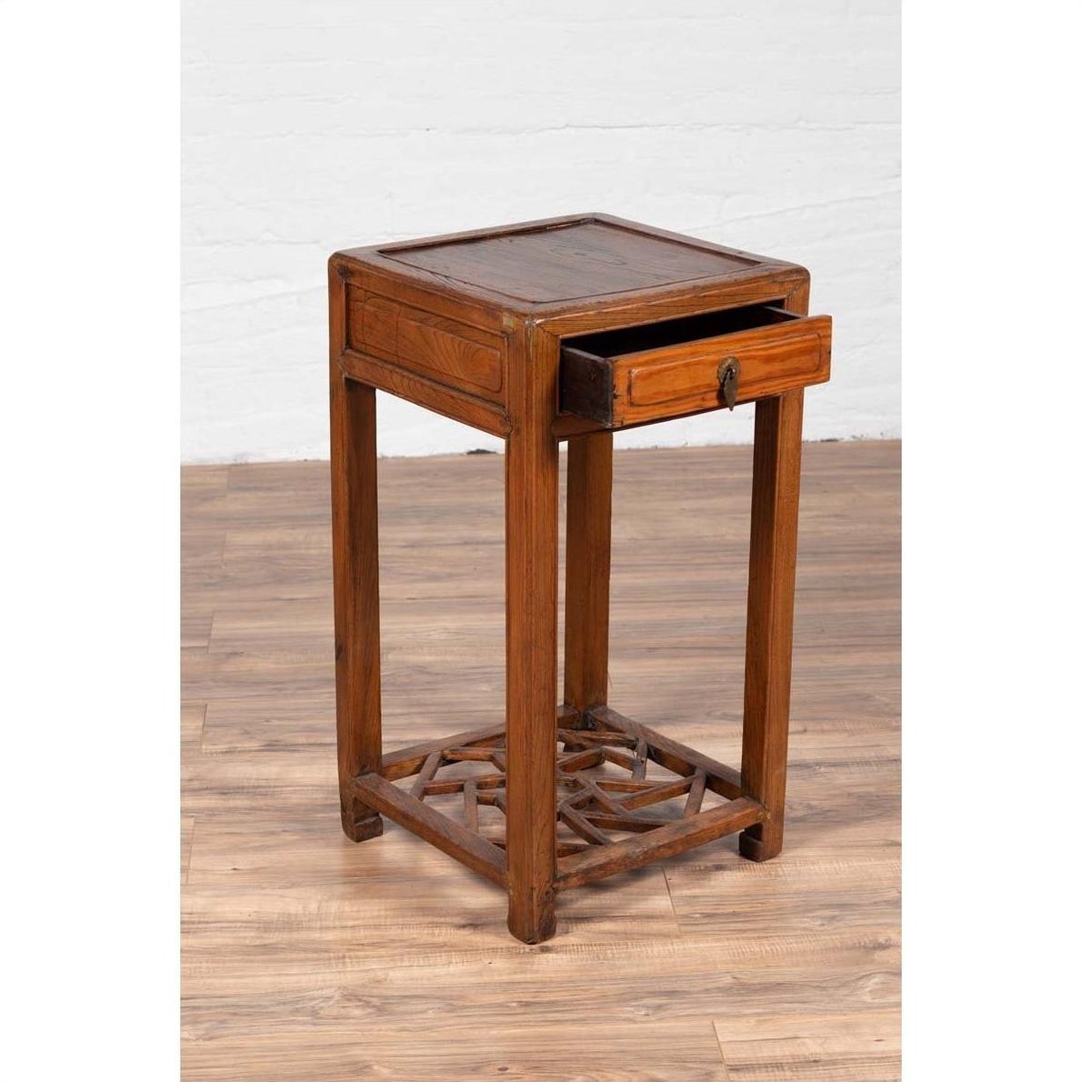Brown elmwood lamp table with single drawer and cracked ice shelf on a wooden floor.