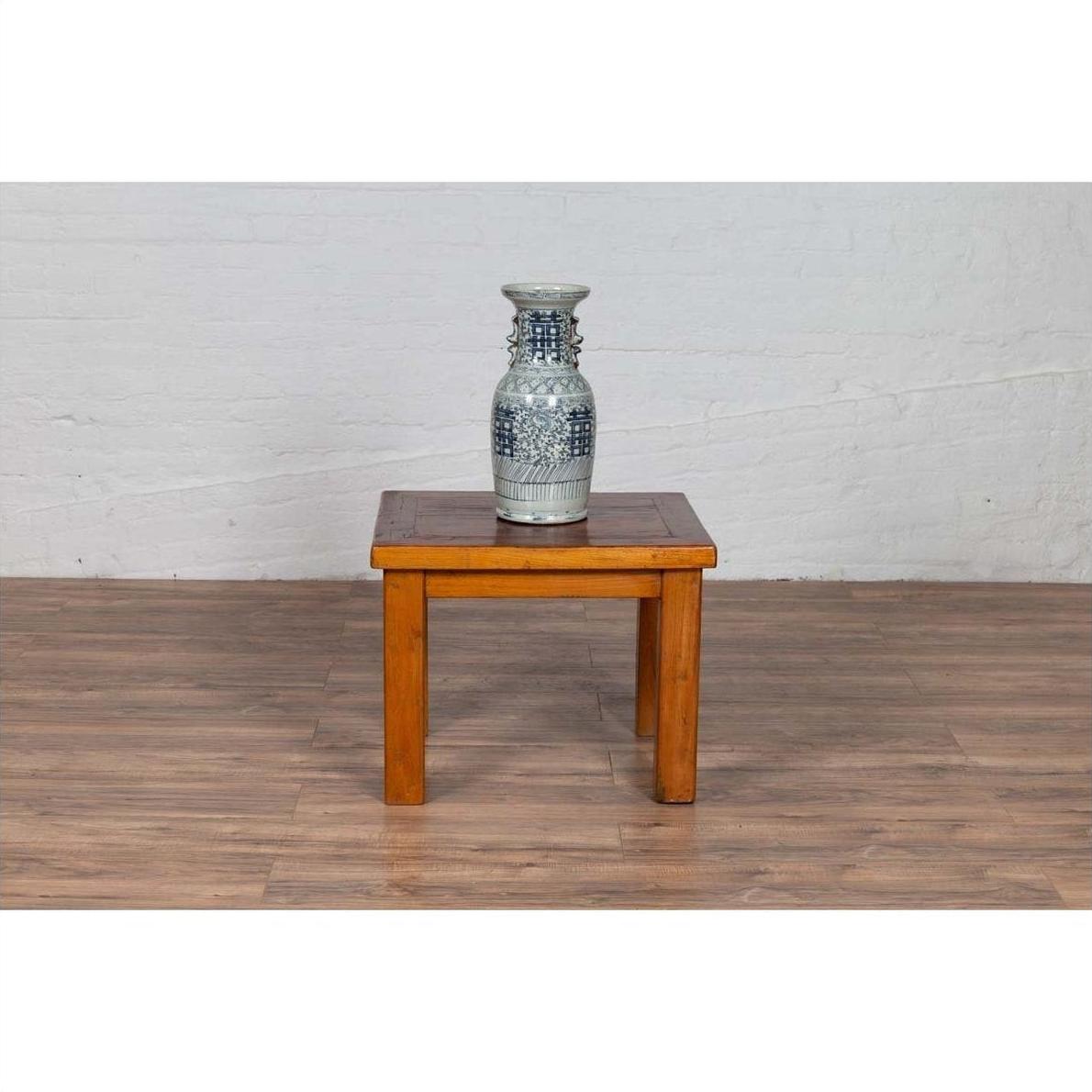 Blue and white ceramic vase on Chinese vintage natural wood side table in front of a white brick wall.