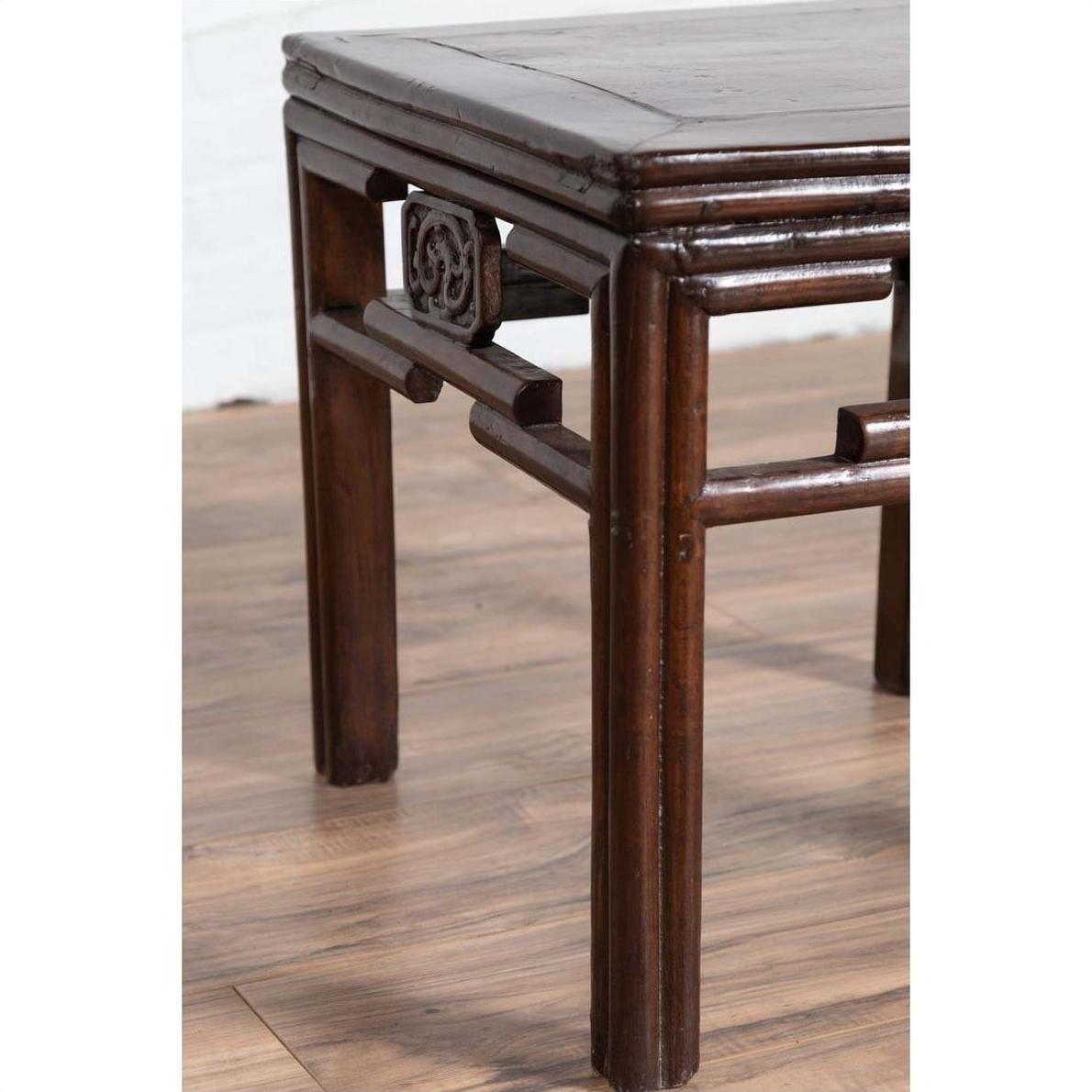Close-up of dark wood Chinese side table leg with carved medallions on a wood-patterned floor.