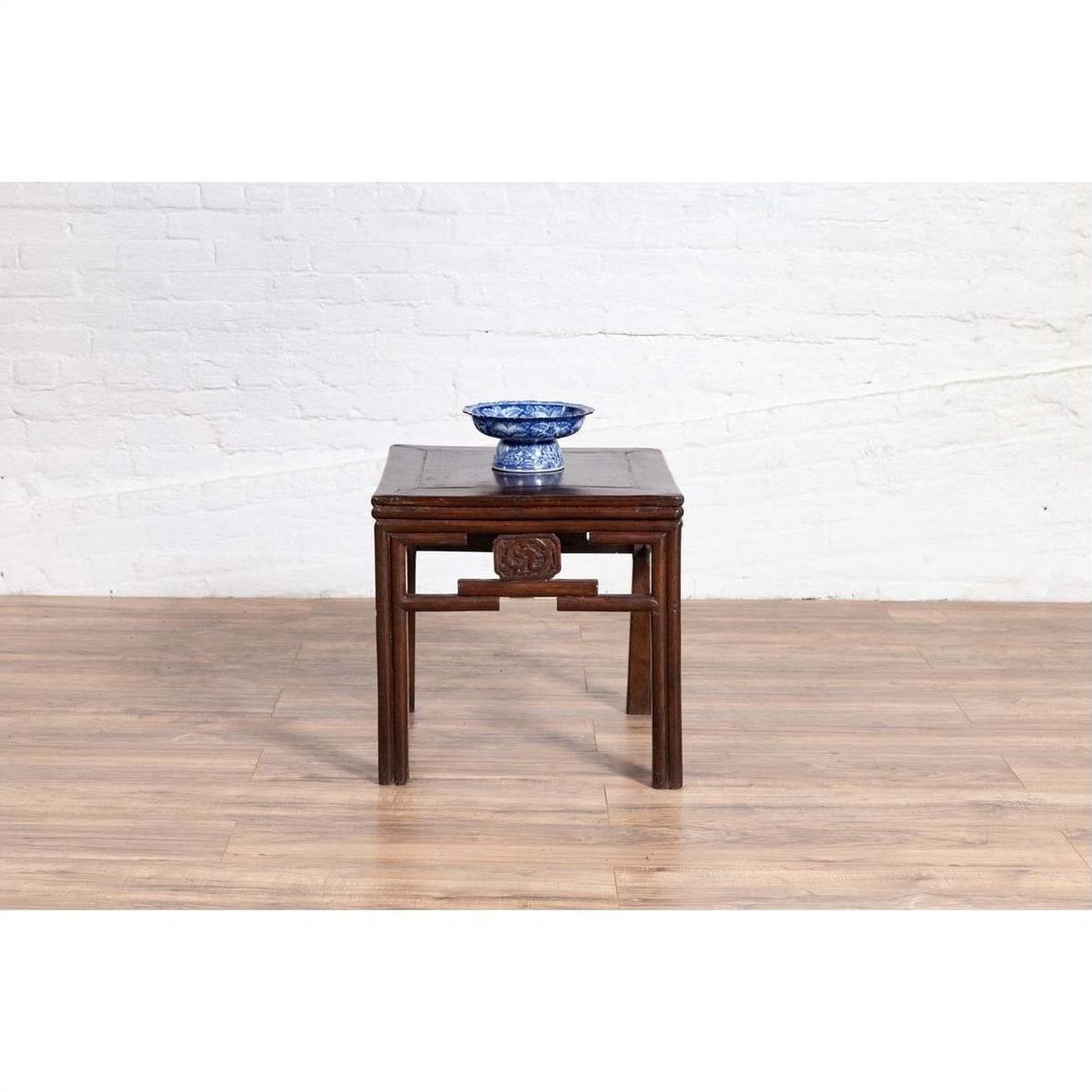 Dark wood side table with carved medallions and dark patina, blue and white bowl on top, indoor setting.