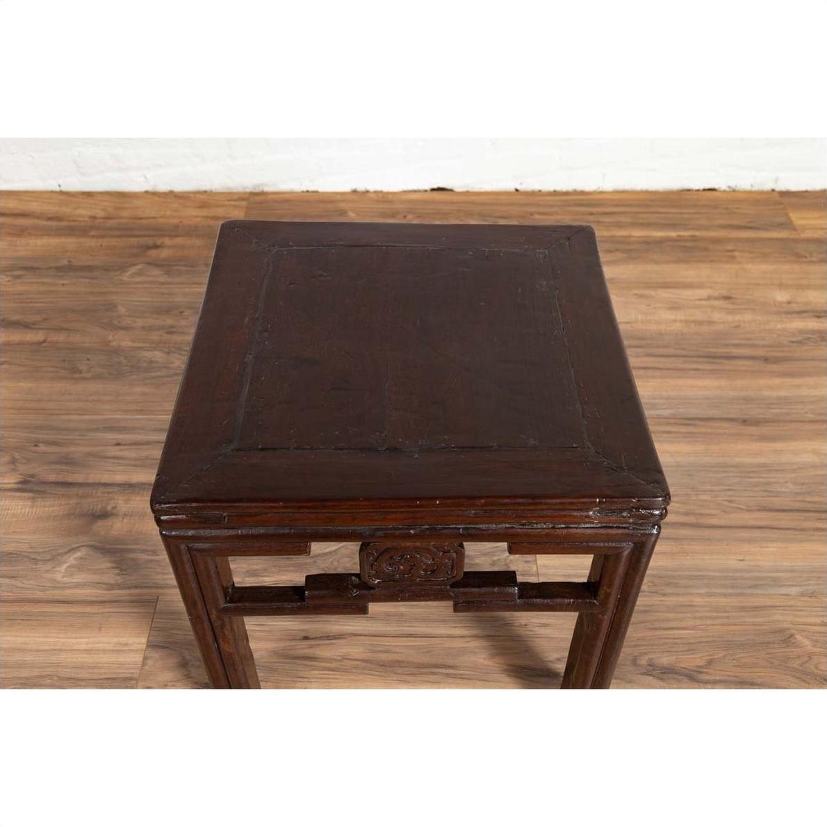 Dark wood Chinese vintage Qing style side table with carved medallions, set on wooden floor by a white wall indoors.