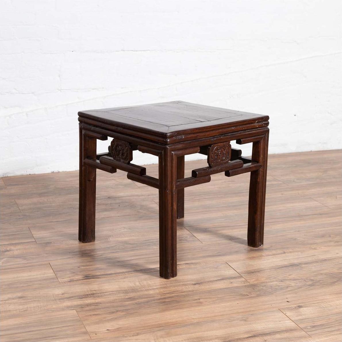 Dark wood side table with carved medallions, vintage Qing style, on wooden floor against a white wall indoors.