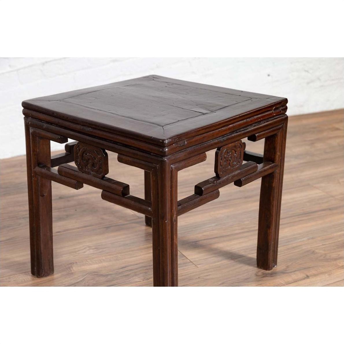 Dark wood Chinese Qing-style side table with carved medallions on light wood floor against white wall indoors.