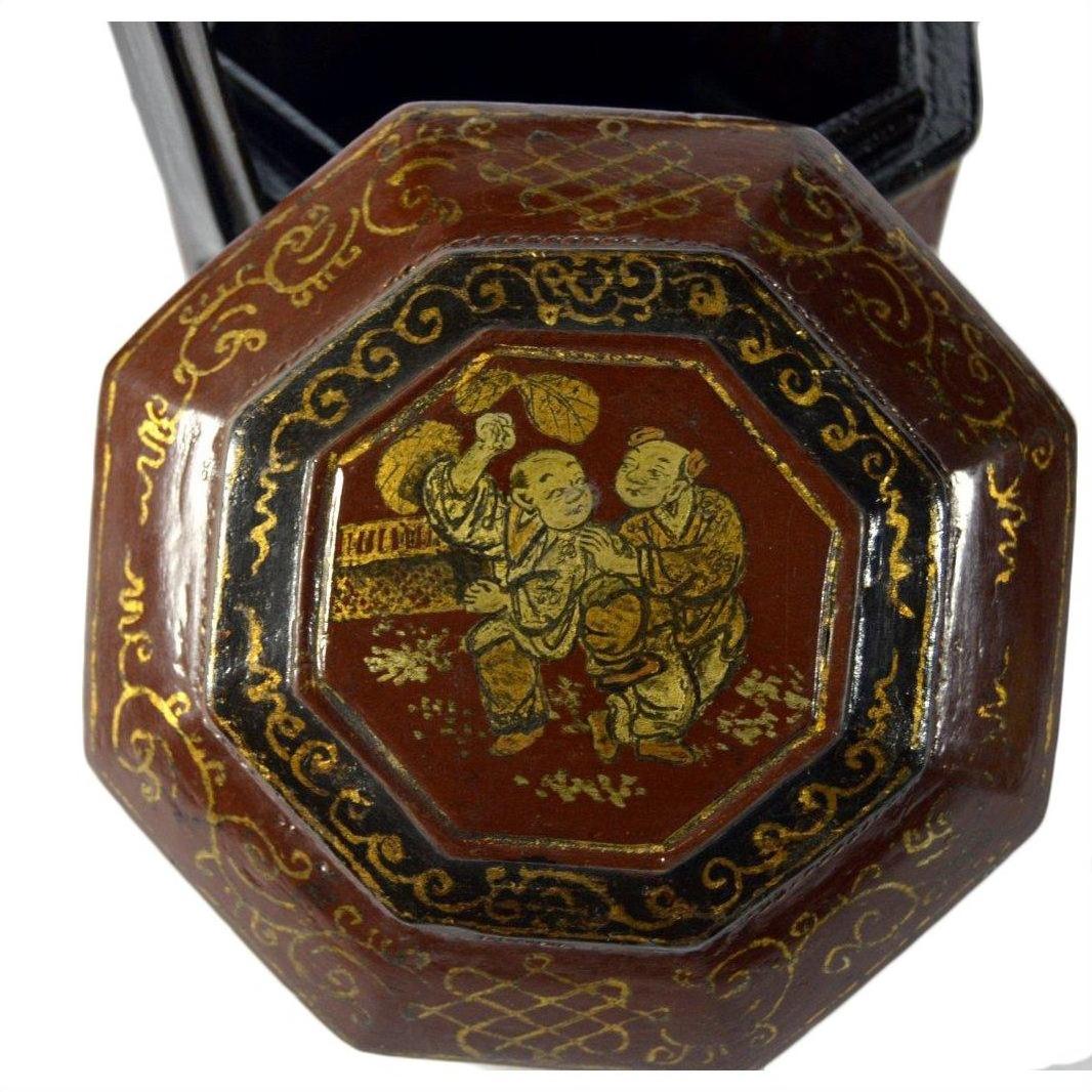 Dark reddish-brown lacquered octagonal Chinese wedding basket with gilt ornate figures and patterns, close-up view.