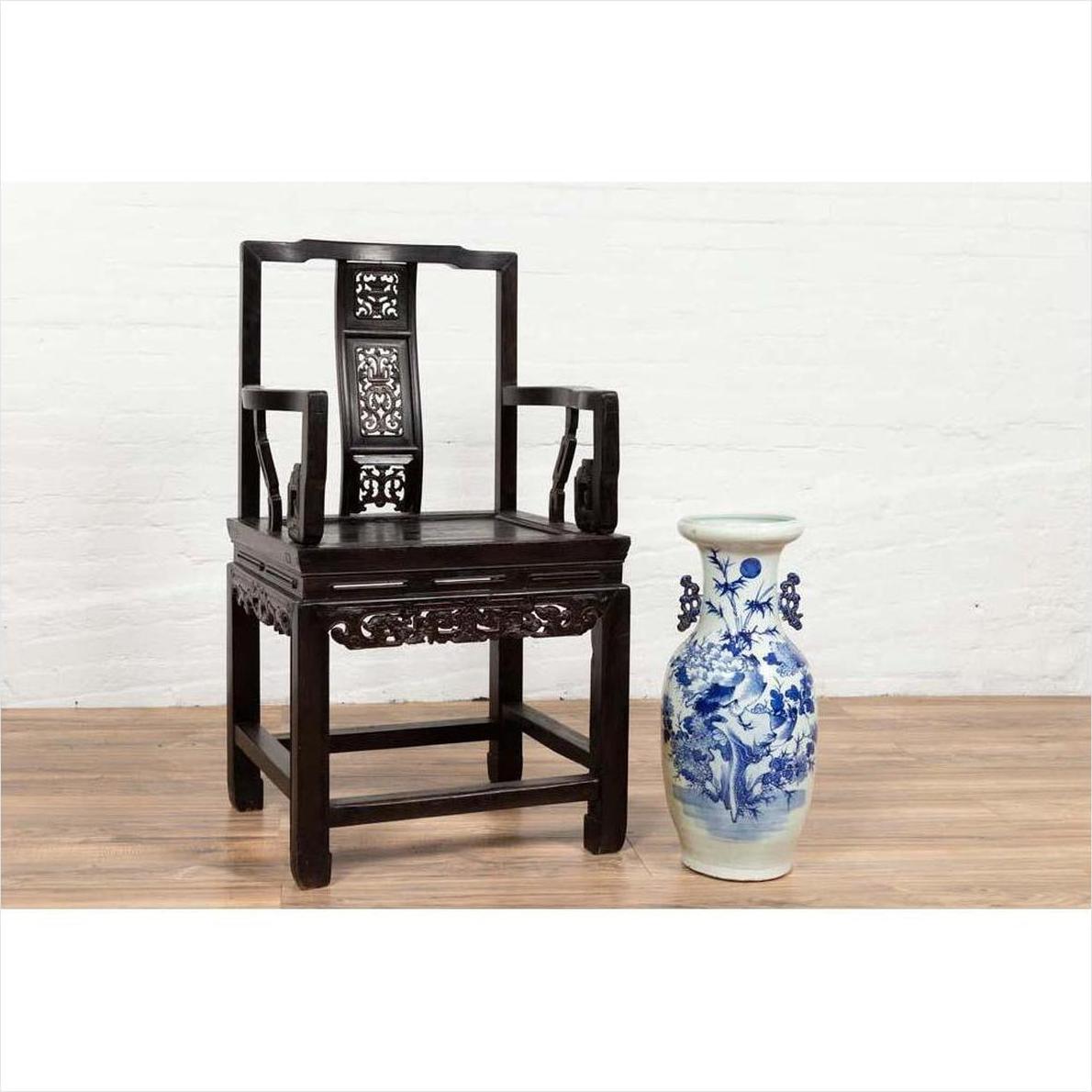 Dark wood Chinese wedding chair with curved pierced splat, serpentine arms, next to blue and white ceramic vase on wood floor.