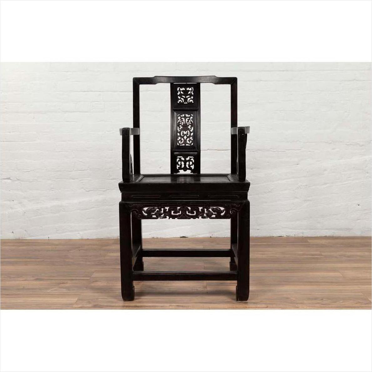 Dark wood Chinese Wedding Chair with curvy pierced splat and serpentine arms on wooden floor by white brick wall.