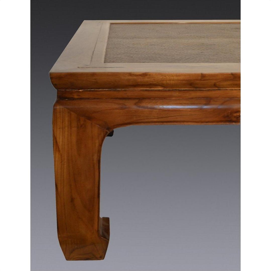 Close-up of light lacquered coffee table with curved wooden leg and rattan tabletop inset.