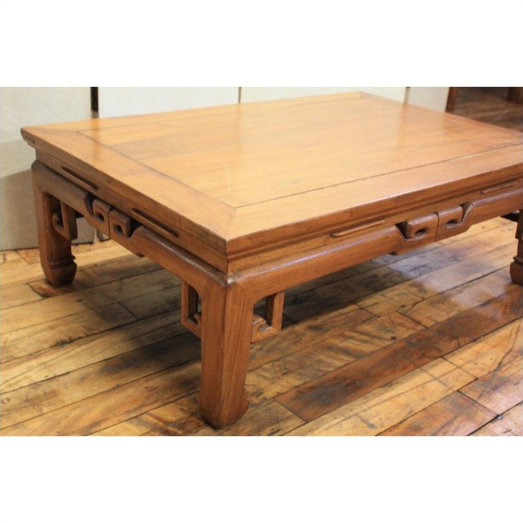 Brown wood coffee table with openwork aprons and carved geometric legs on a hardwood floor.